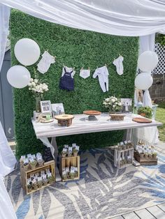 a white table topped with lots of desserts and balloons next to a wall covered in greenery