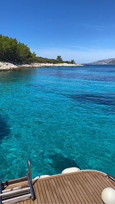 there is a boat that is in the clear blue water near some rocks and trees