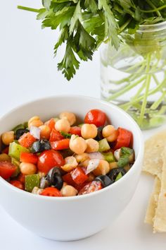 a white bowl filled with vegetables next to tortilla chips and a jar of cilantro