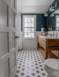 a white toilet sitting next to a bathroom sink under a window on top of a tiled floor