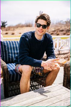 a young man sitting on top of a wooden bench next to a chair and table