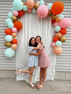 two women standing next to each other in front of a balloon arch