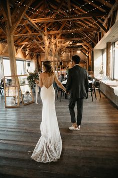 the bride and groom are holding hands in front of an open room with wooden beams