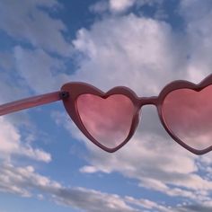 a pair of pink heart shaped sunglasses with clouds in the background