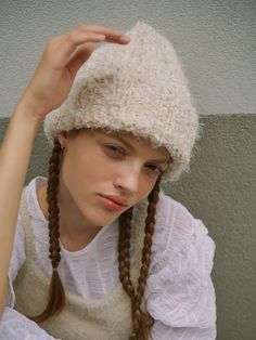 a woman with long braids wearing a white shirt and a knitted hat on her head