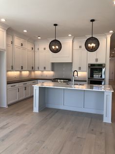 a large kitchen with white cabinets and an island in the middle is lit by two pendant lights