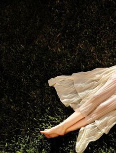 a woman laying in the grass with her legs crossed and wearing a dress that has ruffles on it