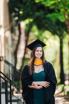 a woman in graduation gown standing on steps with her arms crossed and smiling at the camera