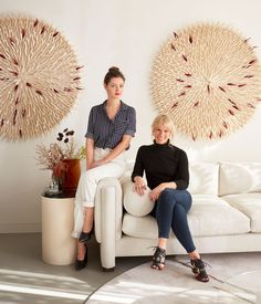 two women sitting on a white couch in front of large wall art hanging above them