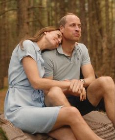 a man and woman sitting on top of a blanket in the woods, cuddling