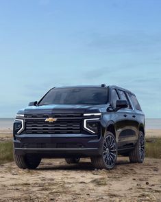 the front end of a black chevrolet suv parked on top of a sandy beach next to the ocean