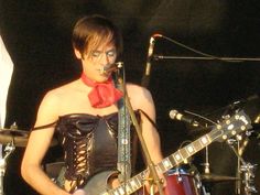 a woman wearing a corset and holding a guitar in front of a microphone