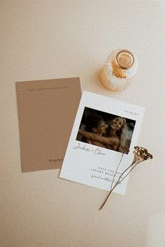 an open photo album next to a vase with dried flowers and a card on it