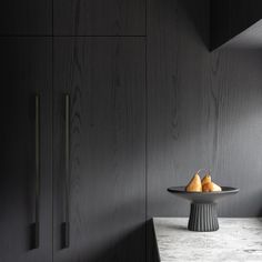 two pears in a bowl on a table next to black cabinets and cupboards