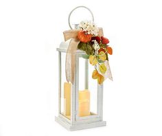 a white lantern with some flowers and candles in it on a white background, there is a bow tied around the candle