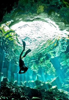 a person swimming in an underwater cave with sunlight streaming through the water's surface