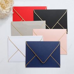 four different colored envelopes on a white surface with flowers in the corner and one is open