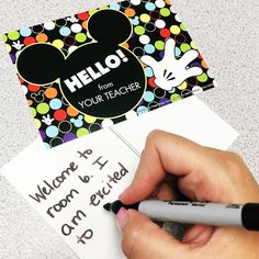 a person writing on a mickey mouse notepad with a black marker and a hello from your teacher sticker next to it