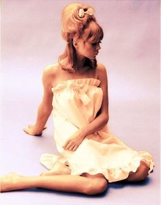 a woman sitting on the floor in a white dress with her legs crossed, looking down