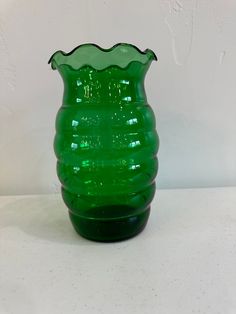 a green glass vase sitting on top of a white tableclothed floor next to a wall