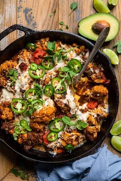 a skillet filled with chicken and vegetables on top of a wooden table next to sliced avocado