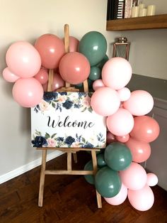 a welcome sign is surrounded by balloons in pastel pink, green and grey colors