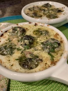 two white dishes filled with food sitting on top of a green place mat next to each other