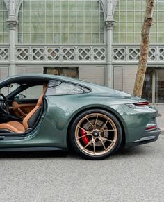 a green sports car parked in front of a building with its door open and the driver's seat up