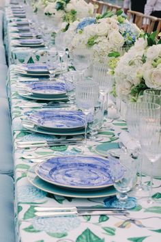 the table is set with blue and white plates, silverware, and vases