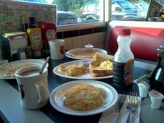 two plates of breakfast food on a table in front of a window with cars outside