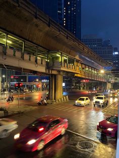 cars are driving down the street at night in an urban area with high rise buildings