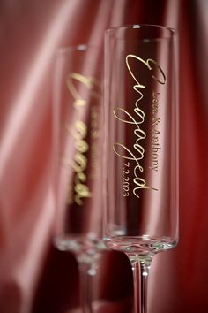 two wine glasses sitting on top of a table next to a red cloth covered wall