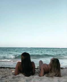 two women laying in the sand at the beach