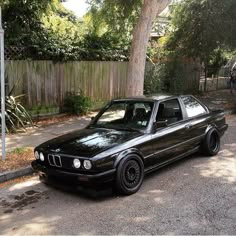 the black car is parked on the side of the road near a tree and fence