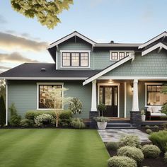 a green house with white trim and black shingles on the front door, grass in front