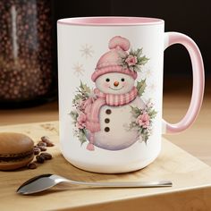 a pink and white coffee mug with a snowman on it next to a spoon