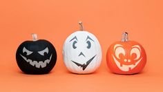 three pumpkins with faces painted on them sitting in front of an orange background,