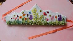 a piece of felt with flowers and bees on it sitting on a pink surface next to a ribbon