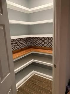 an empty closet with wooden flooring and white shelves on the wall, in front of a door