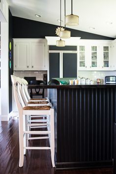 a kitchen with white cabinets and black counter tops next to a bar stool in the middle