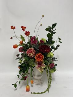 a white vase filled with lots of different colored flowers and greenery next to a candle