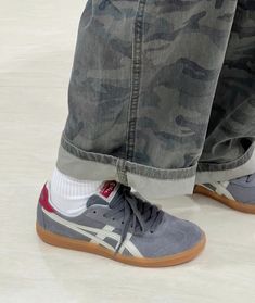 a person wearing grey and white sneakers with camouflage print on the side, standing next to their feet