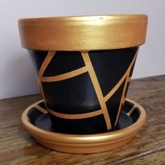 a black and gold pot sitting on top of a wooden table next to a cup