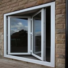 an open white window sitting on top of a wooden floor next to a brick wall