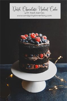 a chocolate cake topped with berries and blueberries on top of a white plate next to a string of lights