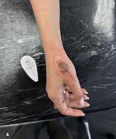 a woman's hand with a small flower tattoo on her left thumb and finger