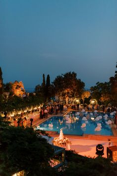 an outdoor pool is lit up at night with people standing around it and lights on the ground