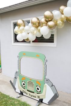 a green and white bus parked in front of a house with balloons hanging from the roof