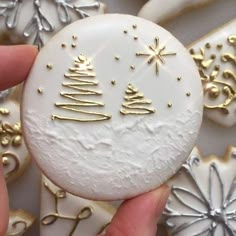 a hand holding a white and gold decorated cookie