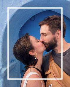 a man and woman kissing each other in front of a blue wall with a white frame